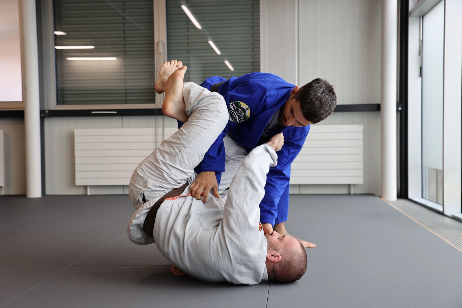 Deux pratiquants en kimono bleu et blanc travaillent une technique de jiu-jitsu sur le tatami de Fight Connect.